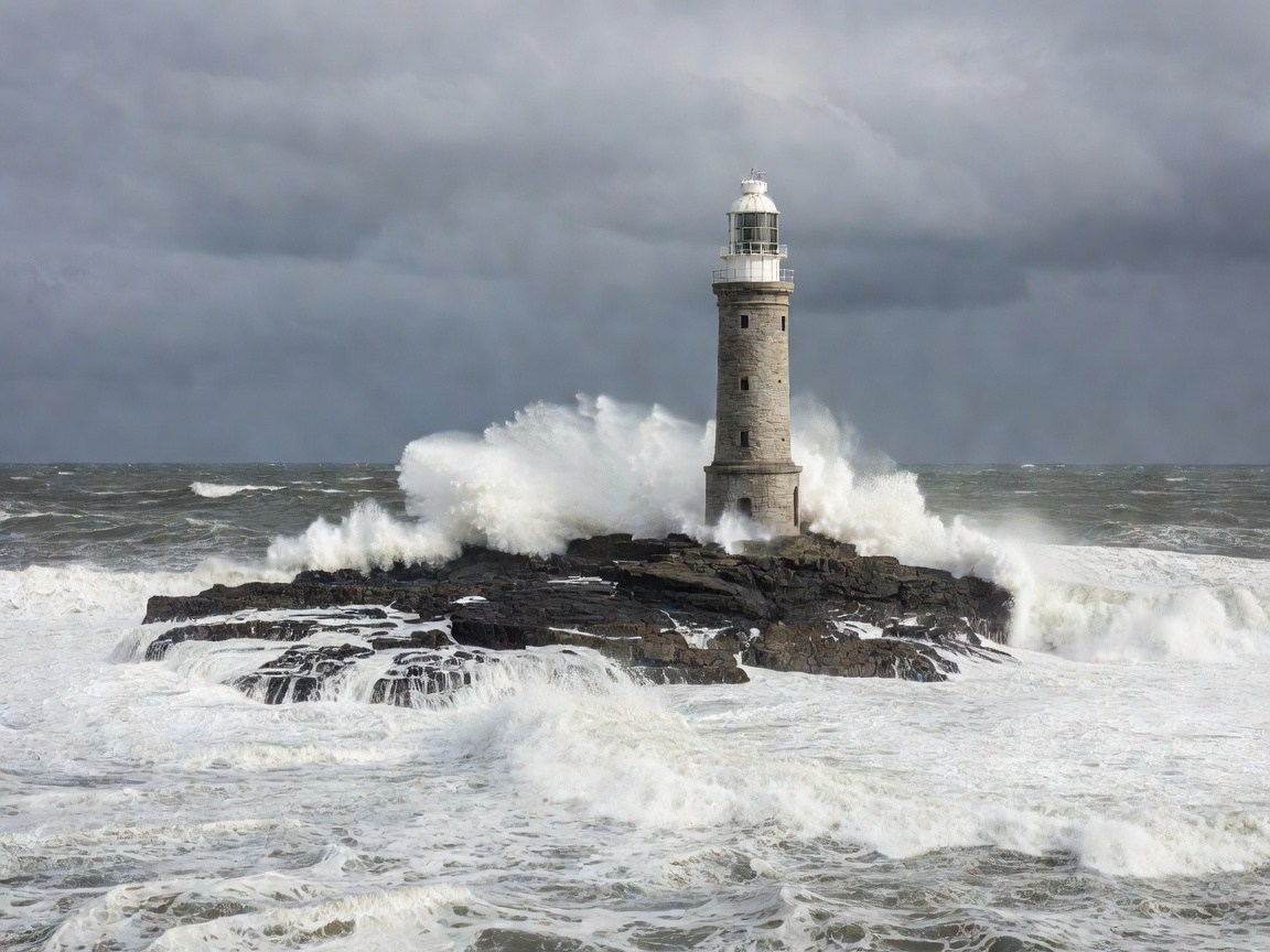 A pale stone lighthouse tower on a low reef with sea breaking around its base